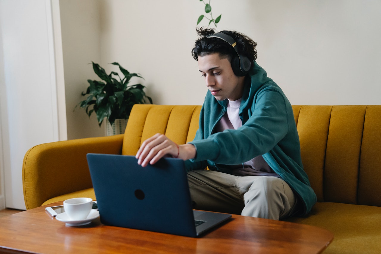 Junger Mann arbeitet von zu Hause aus mit einem Paar Bluetooth-Headsets und einem Laptop